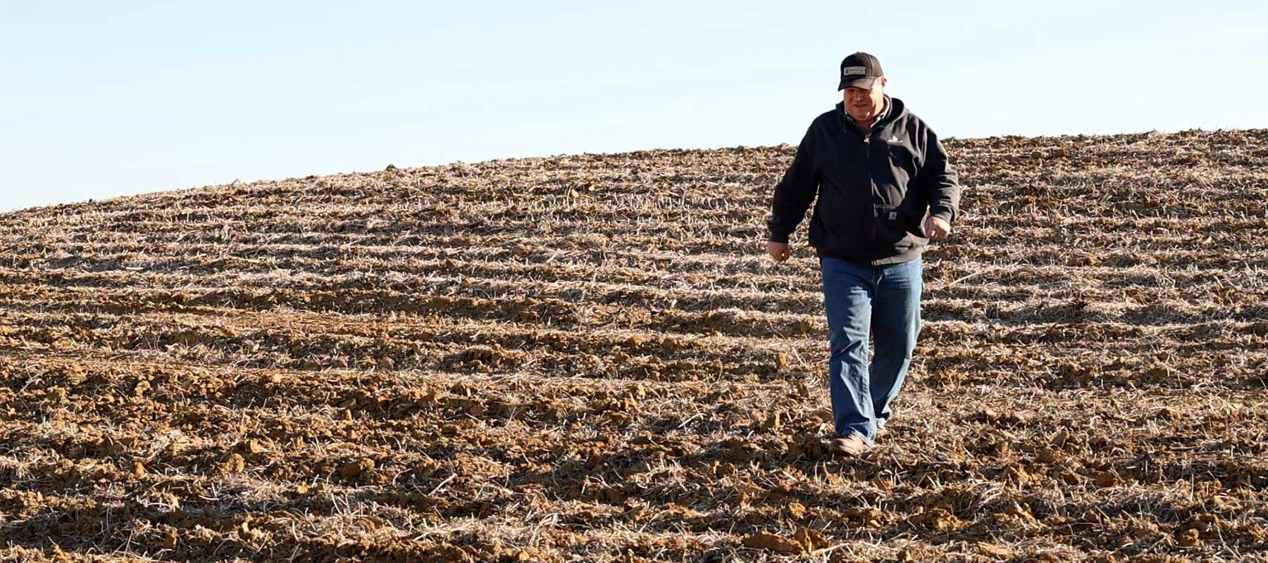 Farmer walking down hill, with crop rows arranged to reduce water erosion. Steve Turner, a farmer in Cass and Mason counties, walks down an example of highly erodible land on farm ground near his home outside Chandlerville. Turner uses cover crops, grass waterways, residue management and other conservation techniques.